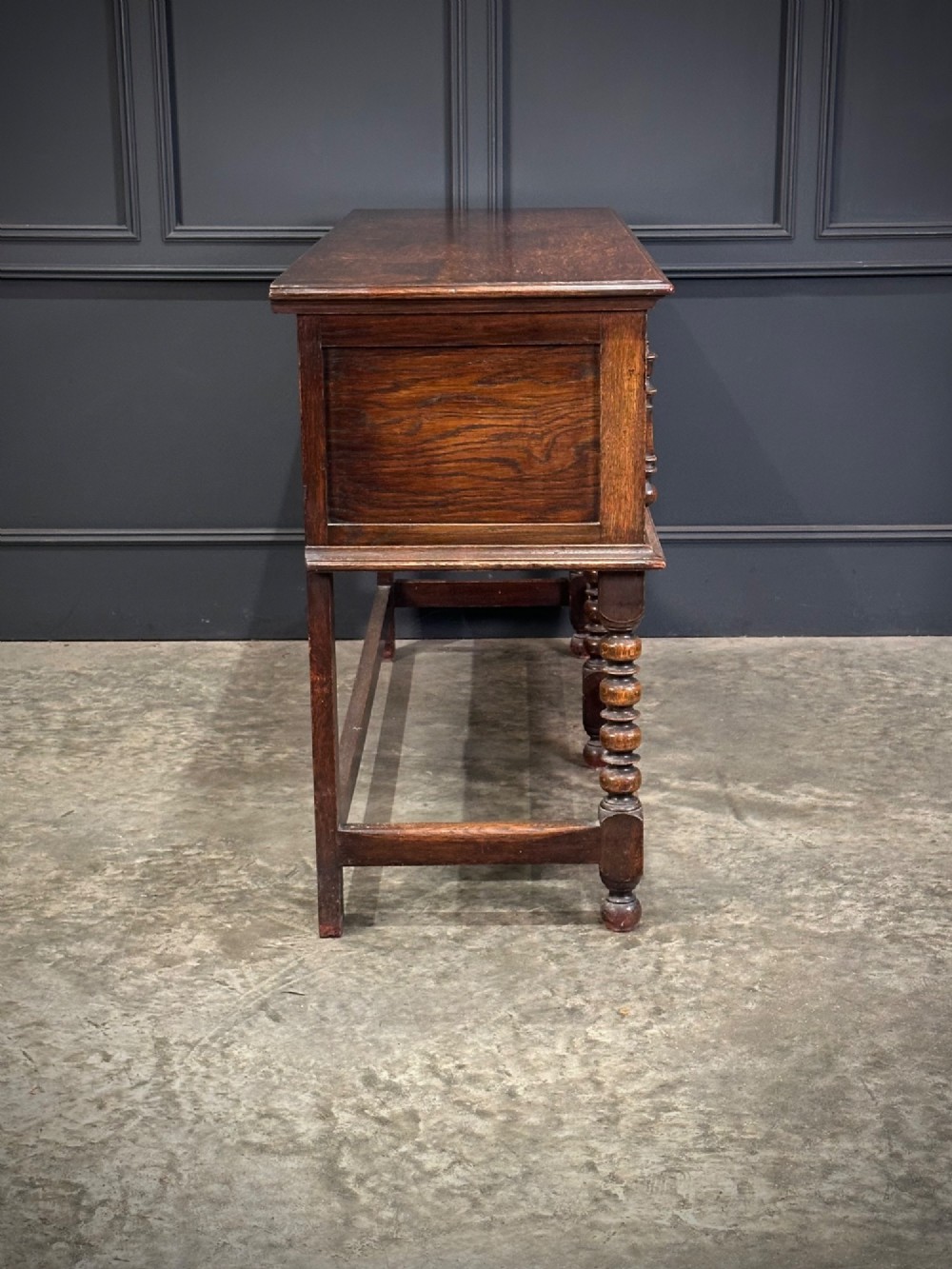 An antique oak dresser base featuring three drawers with geometric panel mouldings, turned front legs, and brass drop handles. View XI