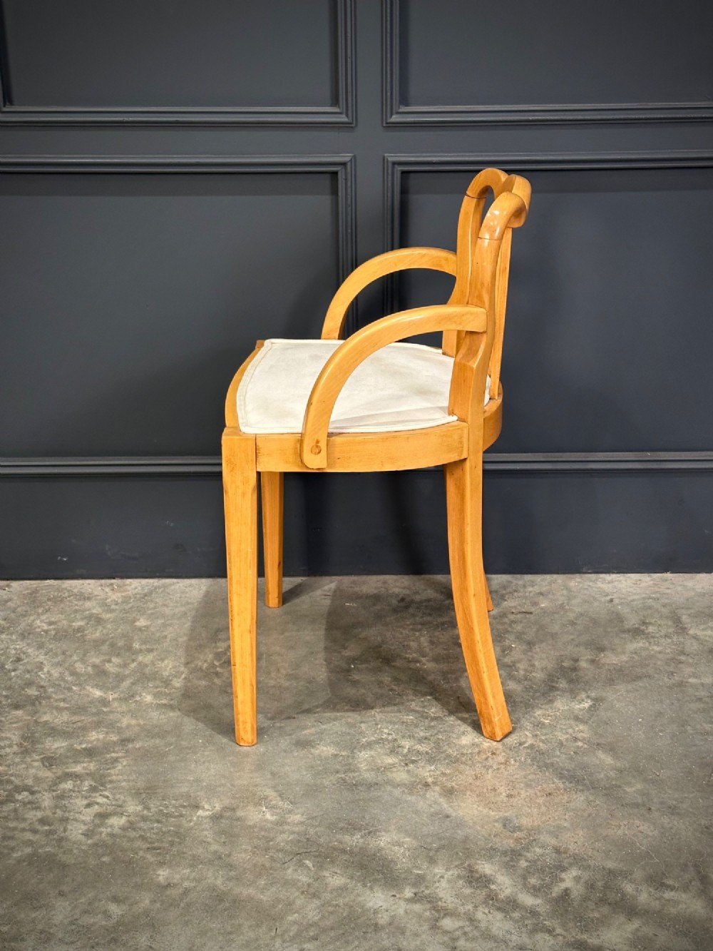 An Art Deco satinwood armchair featuring a triple-arched back rest, curved sweeping arms, a light cream upholstered seat pad, and tapered legs. View V