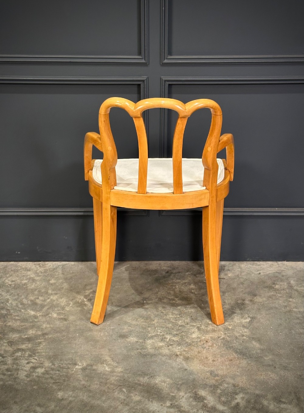 An Art Deco satinwood armchair featuring a triple-arched back rest, curved sweeping arms, a light cream upholstered seat pad, and tapered legs. View VI