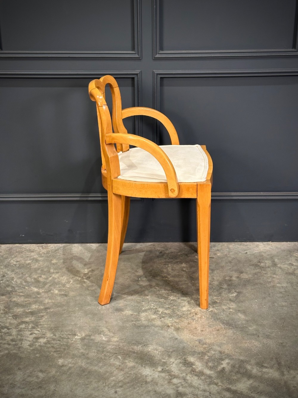 An Art Deco satinwood armchair featuring a triple-arched back rest, curved sweeping arms, a light cream upholstered seat pad, and tapered legs. View VII