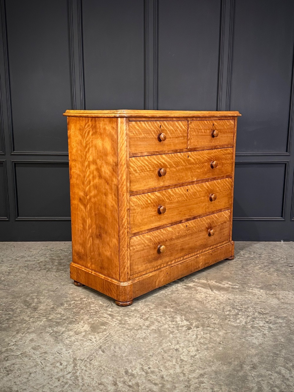 A Victorian satinwood chest of drawers featuring two short drawers over three long drawers with turned wooden knobs and a solid plinth base.