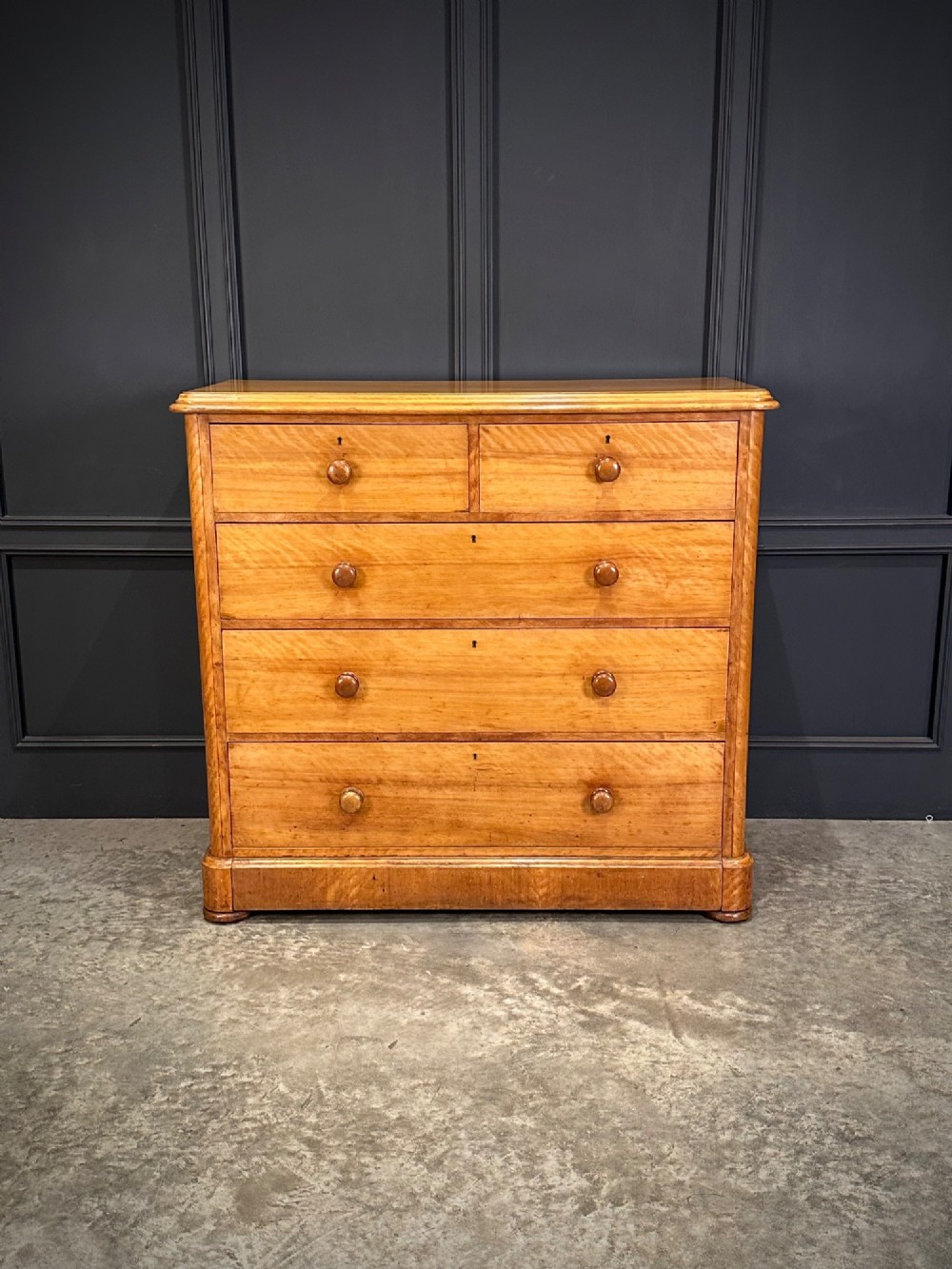A Victorian satinwood chest of drawers featuring two short drawers over three long drawers with turned wooden knobs and a solid plinth base. View IV