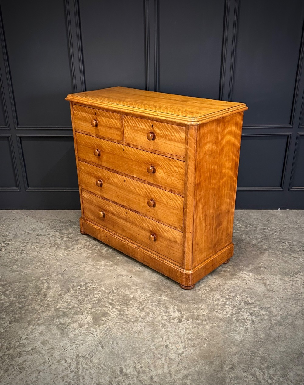 A Victorian satinwood chest of drawers featuring two short drawers over three long drawers with turned wooden knobs and a solid plinth base. View V