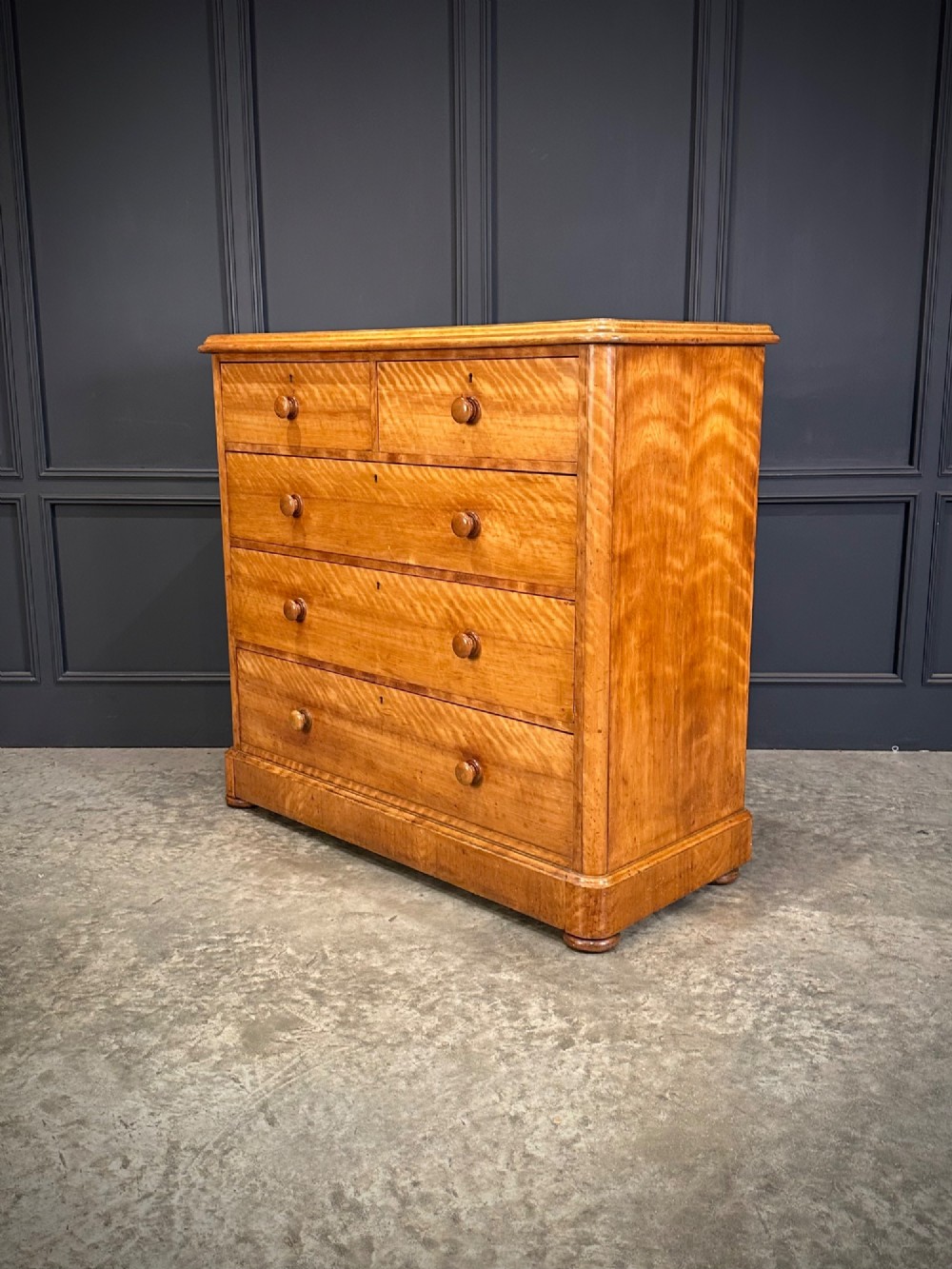 A Victorian satinwood chest of drawers featuring two short drawers over three long drawers with turned wooden knobs and a solid plinth base. View VI