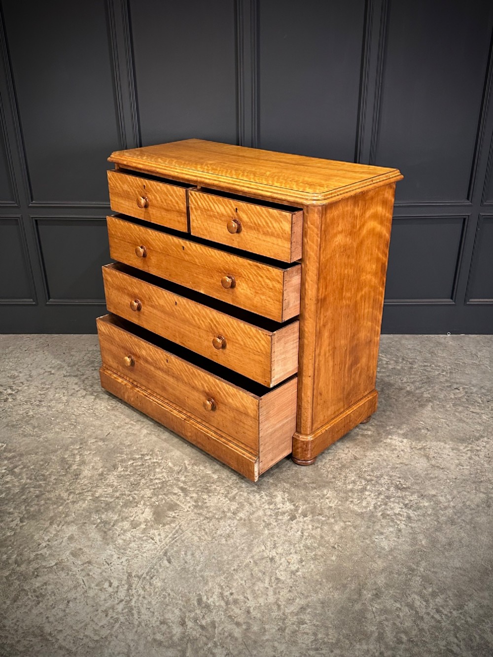 A Victorian satinwood chest of drawers featuring two short drawers over three long drawers with turned wooden knobs and a solid plinth base. View VII