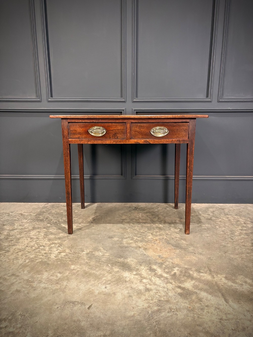 A Georgian mahogany side table featuring two front drawers with oval brass handles and straight square tapered legs.
