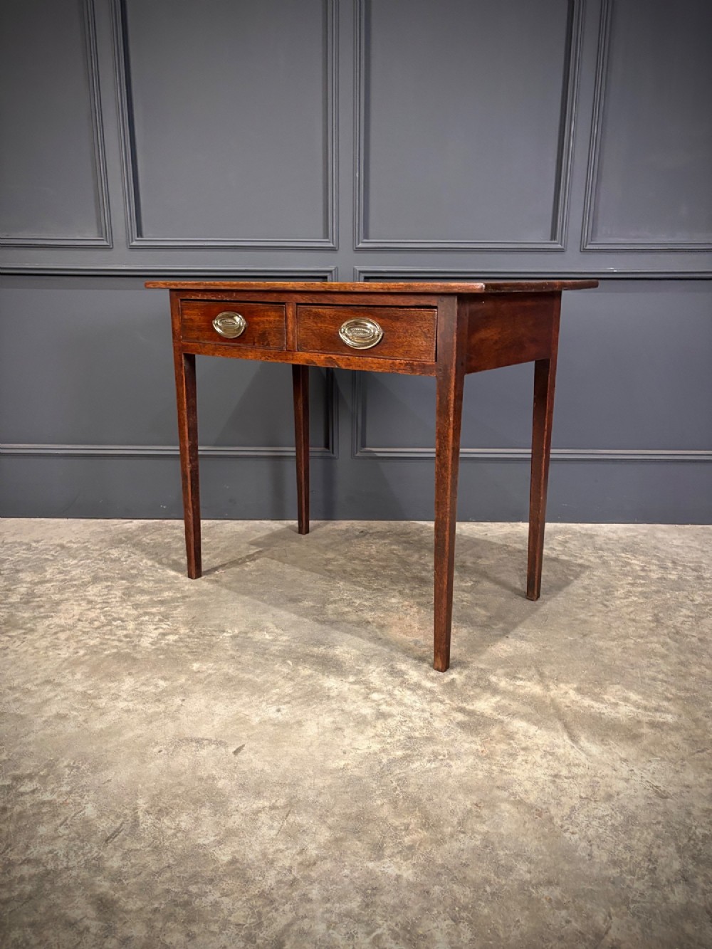 A Georgian mahogany side table featuring two front drawers with oval brass handles and straight square tapered legs. View VI