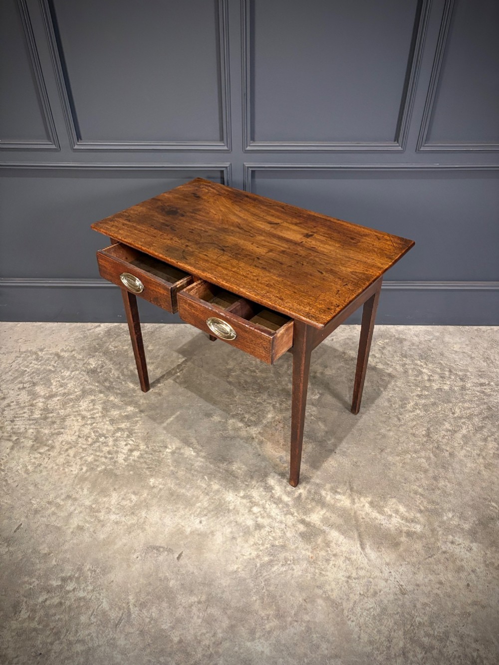 A Georgian mahogany side table featuring two front drawers with oval brass handles and straight square tapered legs. View VII
