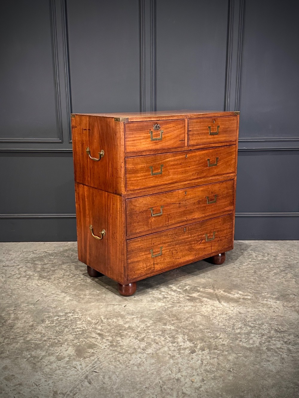 A Victorian two-part mahogany military campaign chest featuring flush brass handles, brass corner mounts, and turned bun feet.