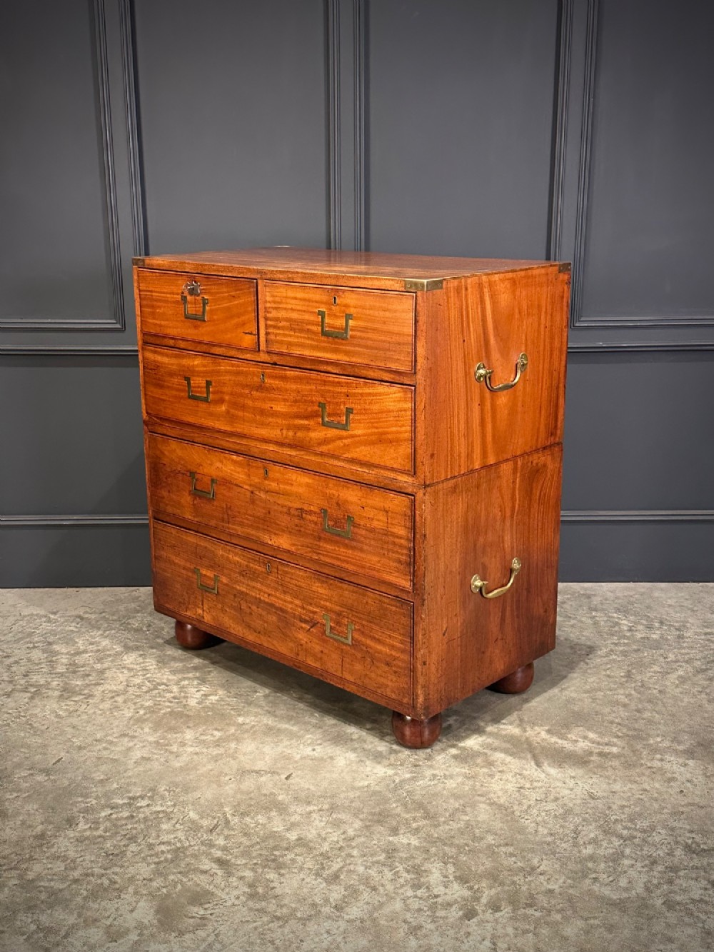 A Victorian two-part mahogany military campaign chest featuring flush brass handles, brass corner mounts, and turned bun feet. View VI