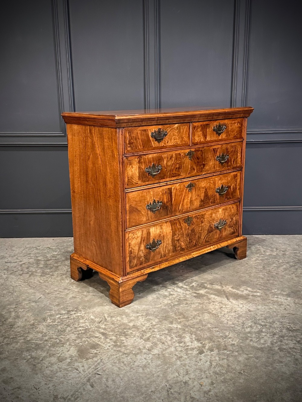An 18th-century walnut chest of drawers featuring two short drawers over three long drawers, brass handles, and bracket feet.