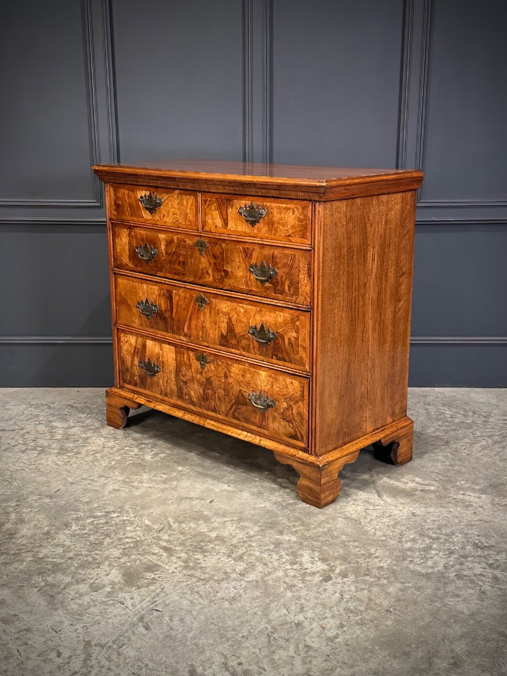 An 18th-century walnut chest of drawers featuring two short drawers over three long drawers, brass handles, and bracket feet. View V