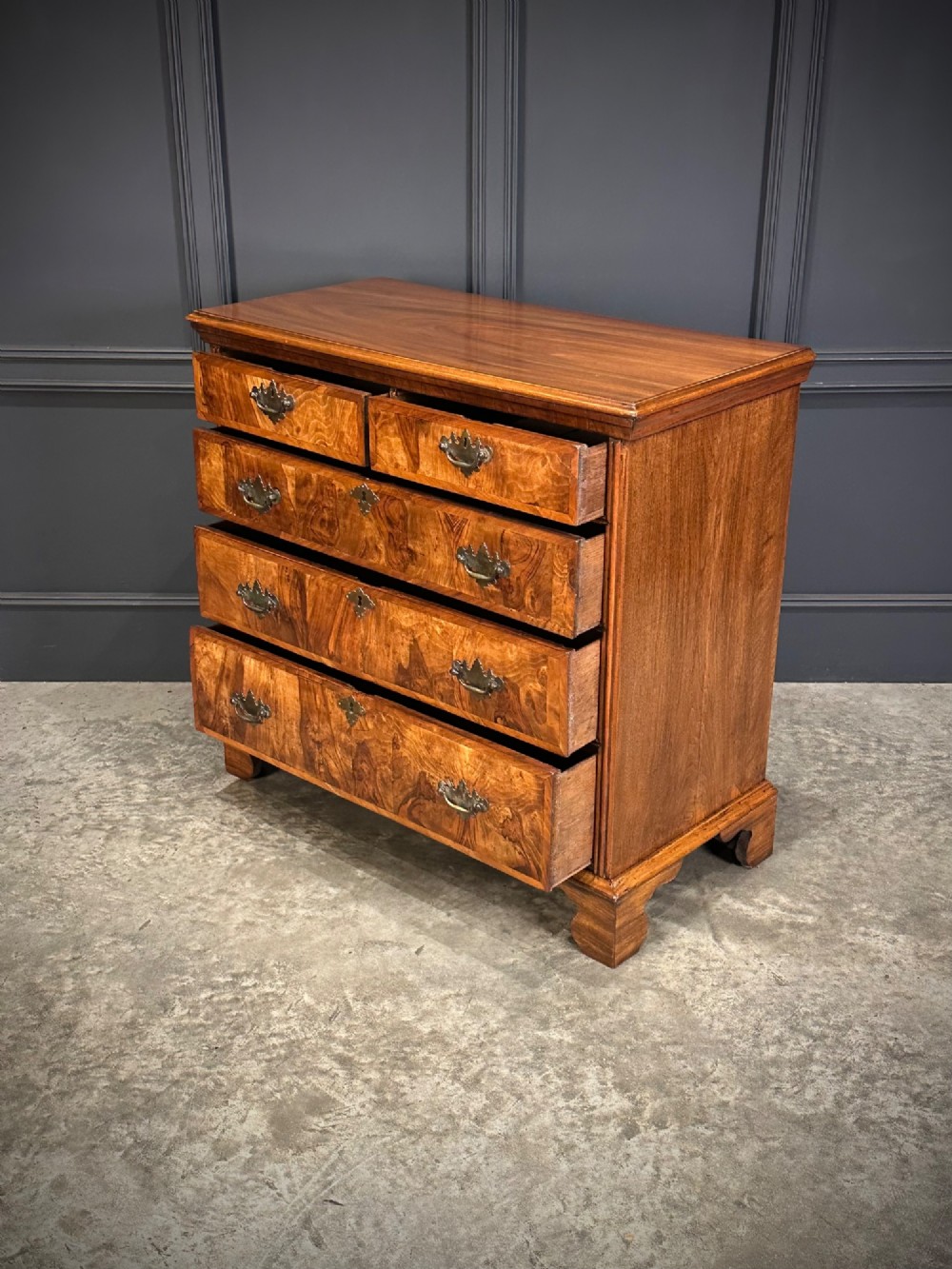 An 18th-century walnut chest of drawers featuring two short drawers over three long drawers, brass handles, and bracket feet. View VI