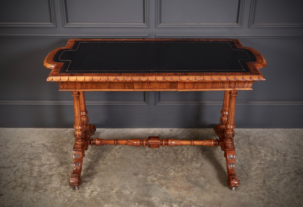 A carved walnut library table featuring a dark leather inset writing surface, detailed apron moulding, turned twin supports, and a carved trestle base with scroll feet. View IV