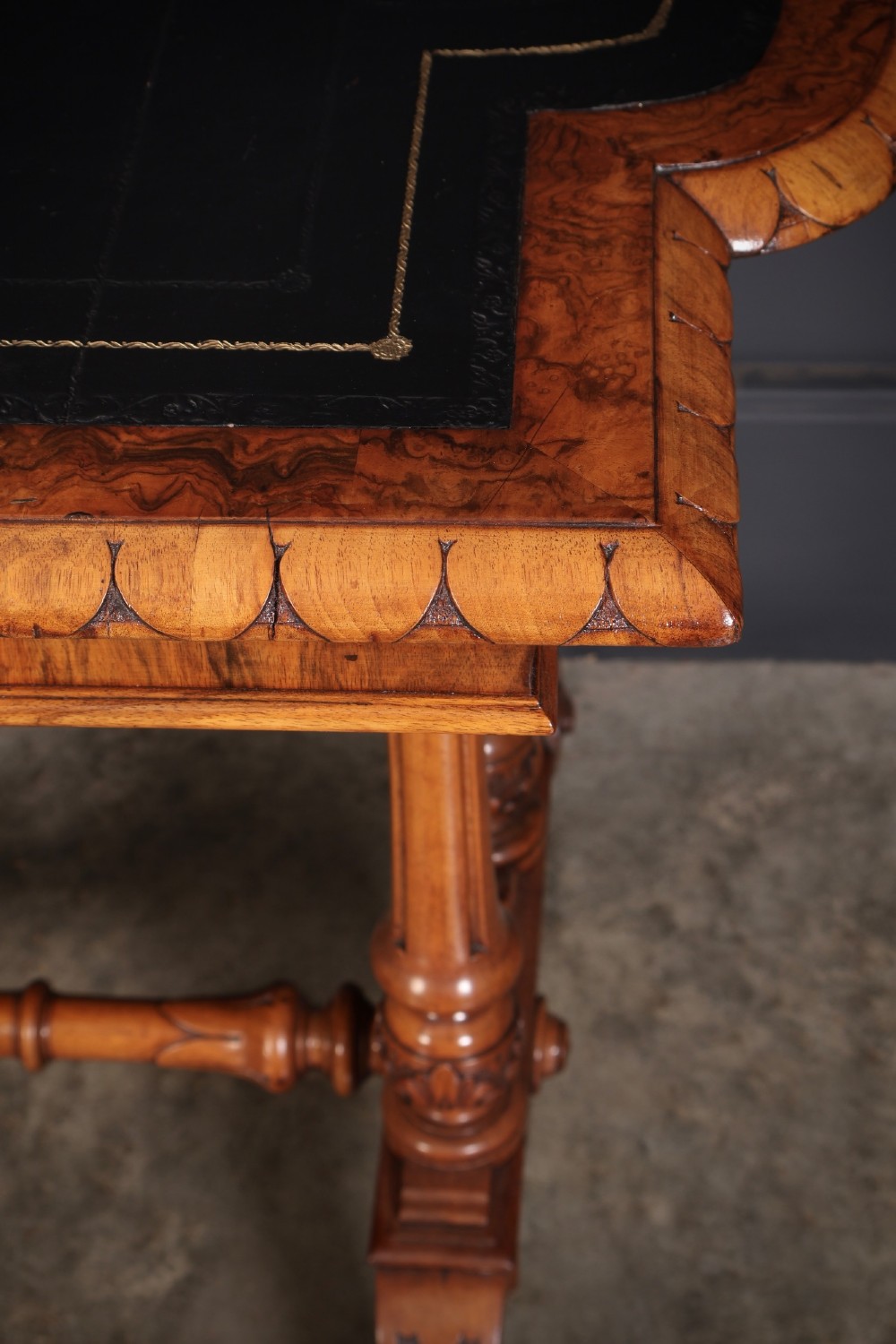 A carved walnut library table featuring a dark leather inset writing surface, detailed apron moulding, turned twin supports, and a carved trestle base with scroll feet. View XIII