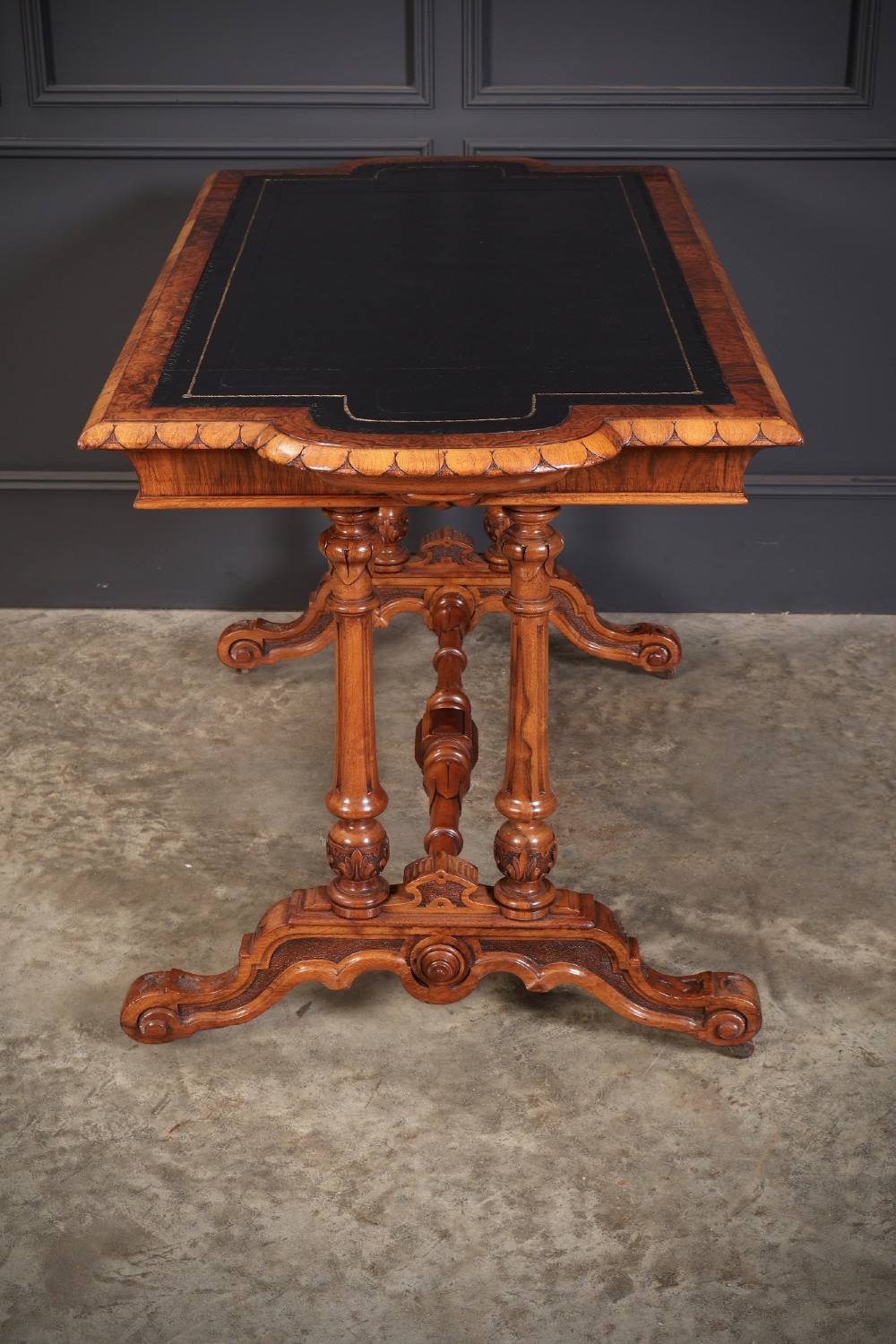 A carved walnut library table featuring a dark leather inset writing surface, detailed apron moulding, turned twin supports, and a carved trestle base with scroll feet. View XIV