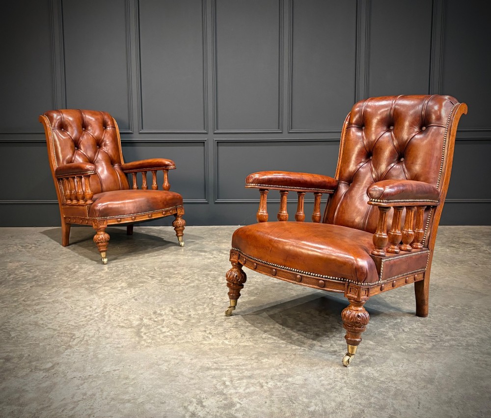 A pair of antique oak armchairs upholstered in deep-buttoned chestnut brown leather with turned front legs and brass castors.
