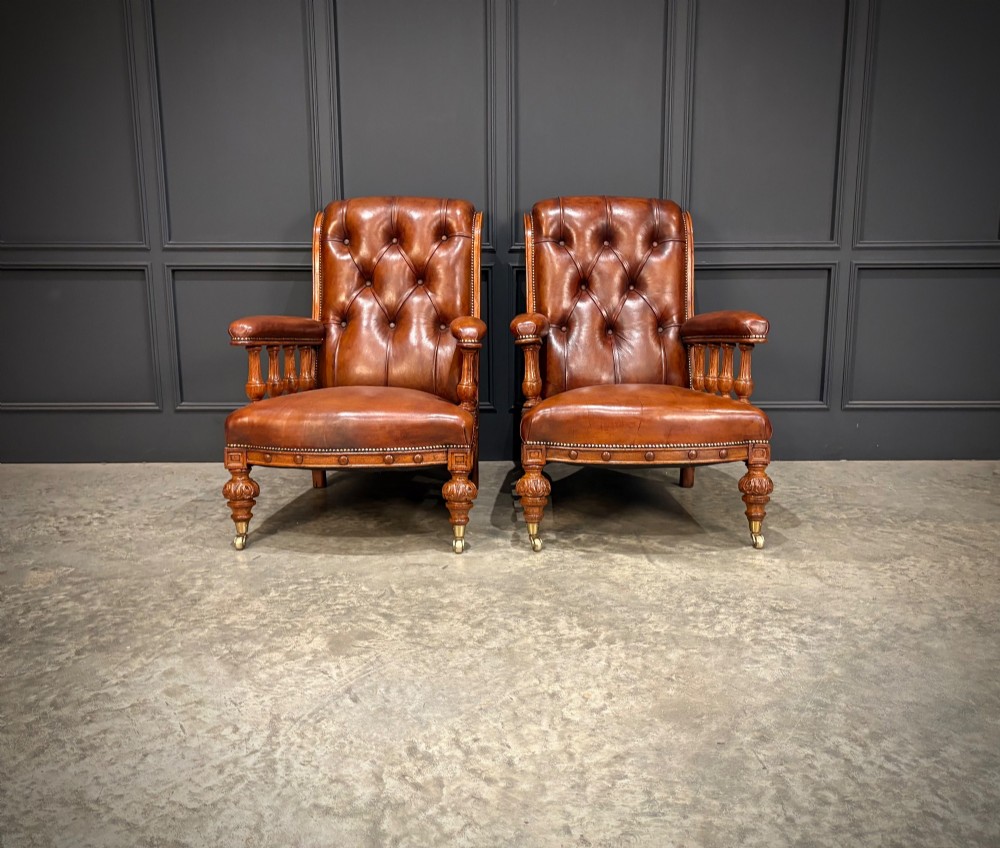A pair of antique oak armchairs upholstered in deep-buttoned chestnut brown leather with turned front legs and brass castors. View II