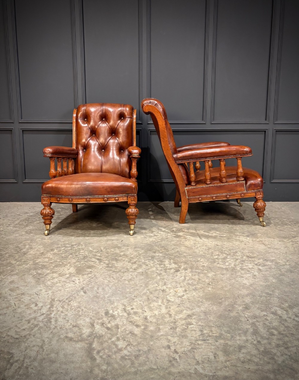 A pair of antique oak armchairs upholstered in deep-buttoned chestnut brown leather with turned front legs and brass castors. View III