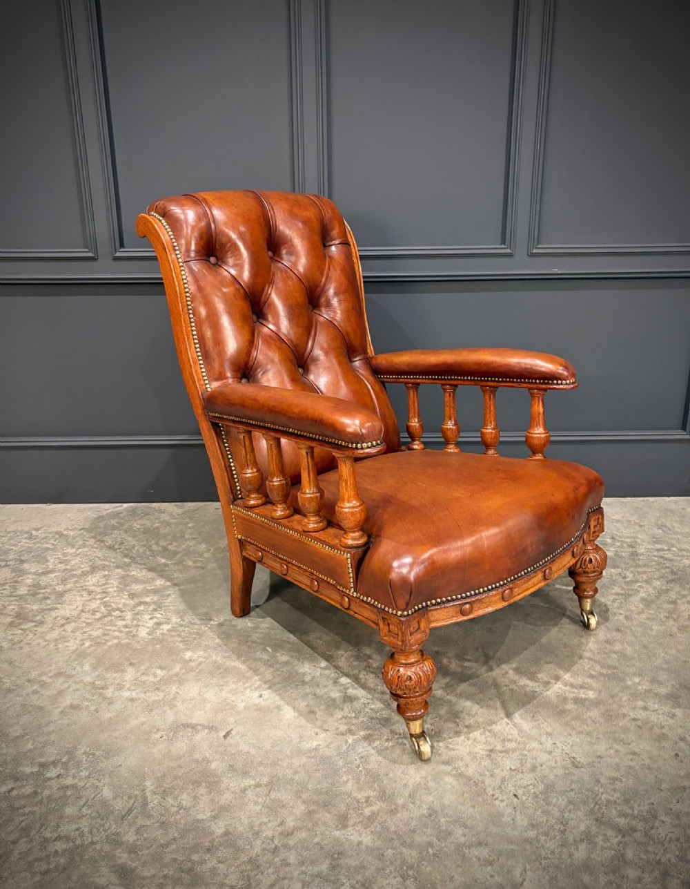 A pair of antique oak armchairs upholstered in deep-buttoned chestnut brown leather with turned front legs and brass castors. View V