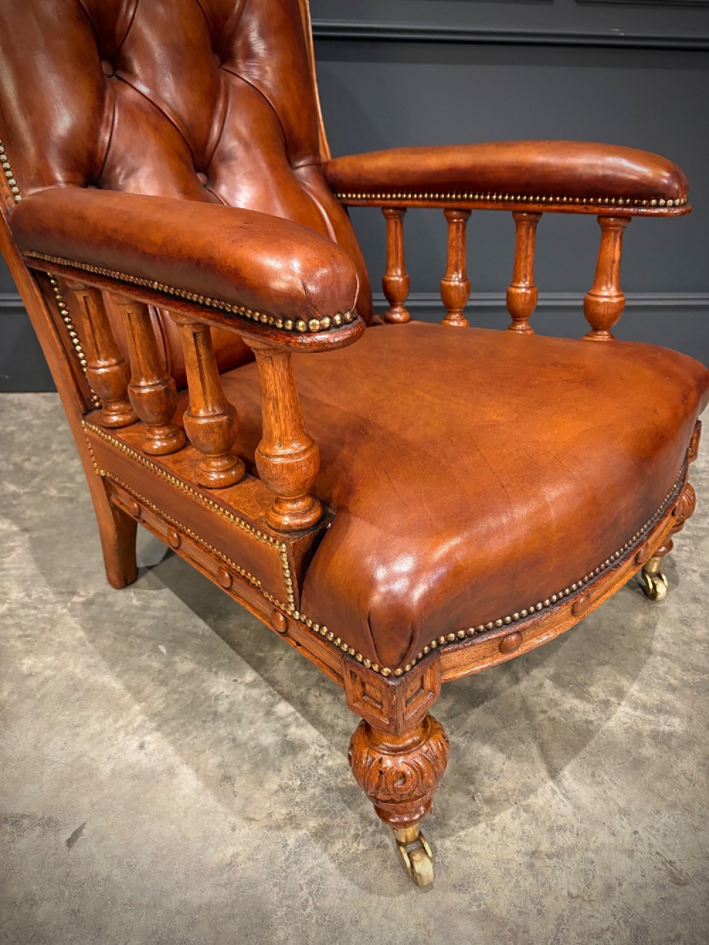 A pair of antique oak armchairs upholstered in deep-buttoned chestnut brown leather with turned front legs and brass castors. View VI