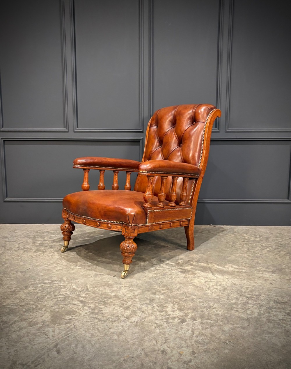 A pair of antique oak armchairs upholstered in deep-buttoned chestnut brown leather with turned front legs and brass castors. View VII