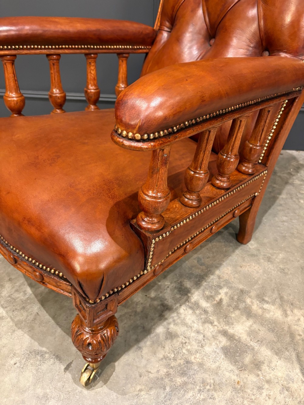 A pair of antique oak armchairs upholstered in deep-buttoned chestnut brown leather with turned front legs and brass castors. View IX