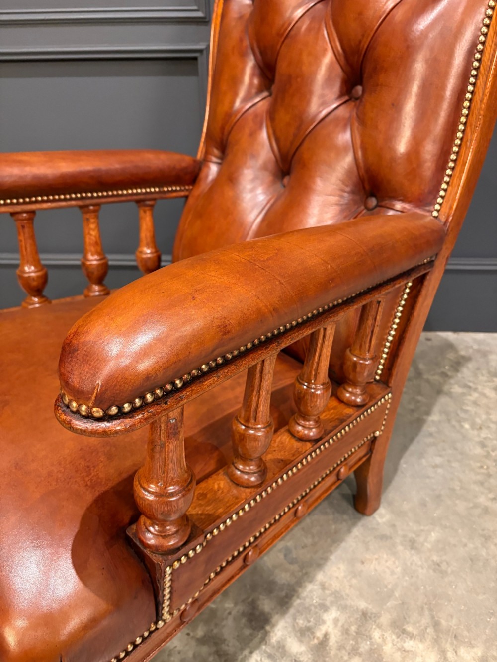 A pair of antique oak armchairs upholstered in deep-buttoned chestnut brown leather with turned front legs and brass castors. View X