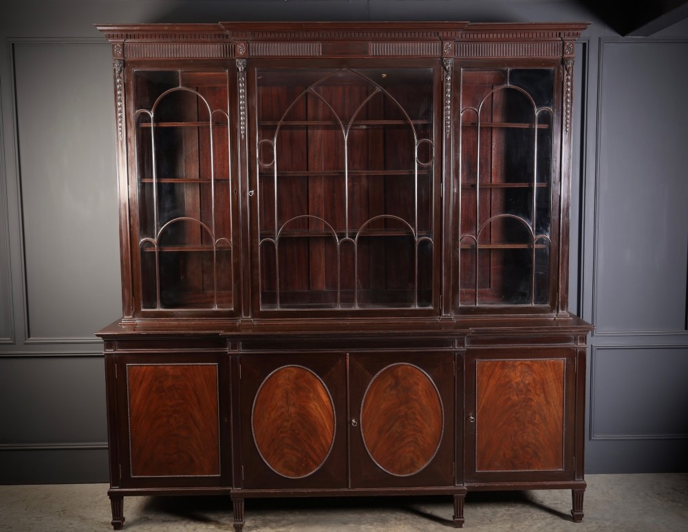 A large mahogany breakfront bookcase featuring upper glazed doors with astragal tracery above lower cupboards with oval flame mahogany veneer panels.