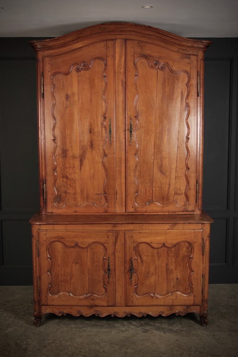 An 18th-century French Provincial two-tier cherry wood cupboard featuring moulded panel doors, long brass hinges, and a curved top cornice. View II