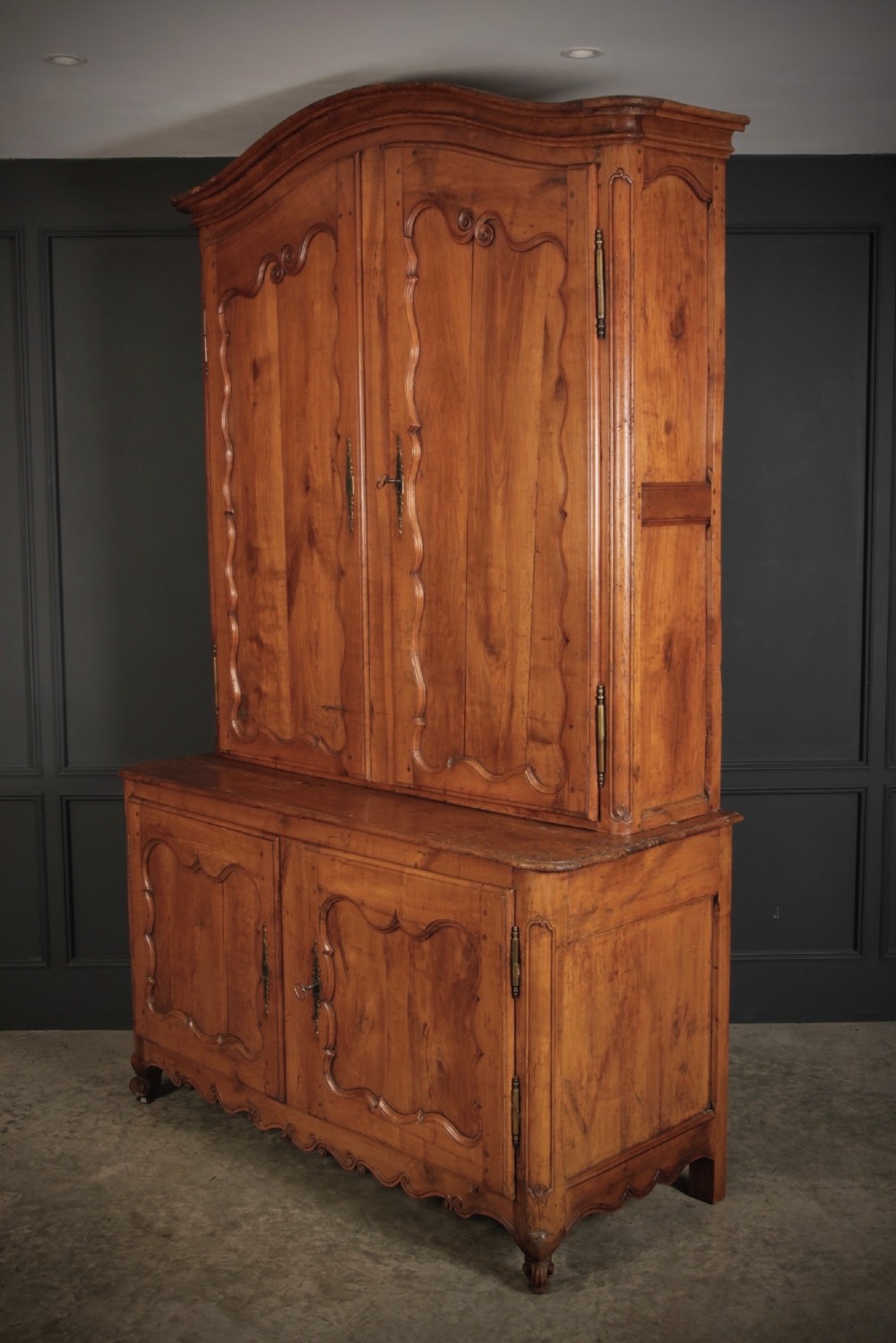 An 18th-century French Provincial two-tier cherry wood cupboard featuring moulded panel doors, long brass hinges, and a curved top cornice. View IV