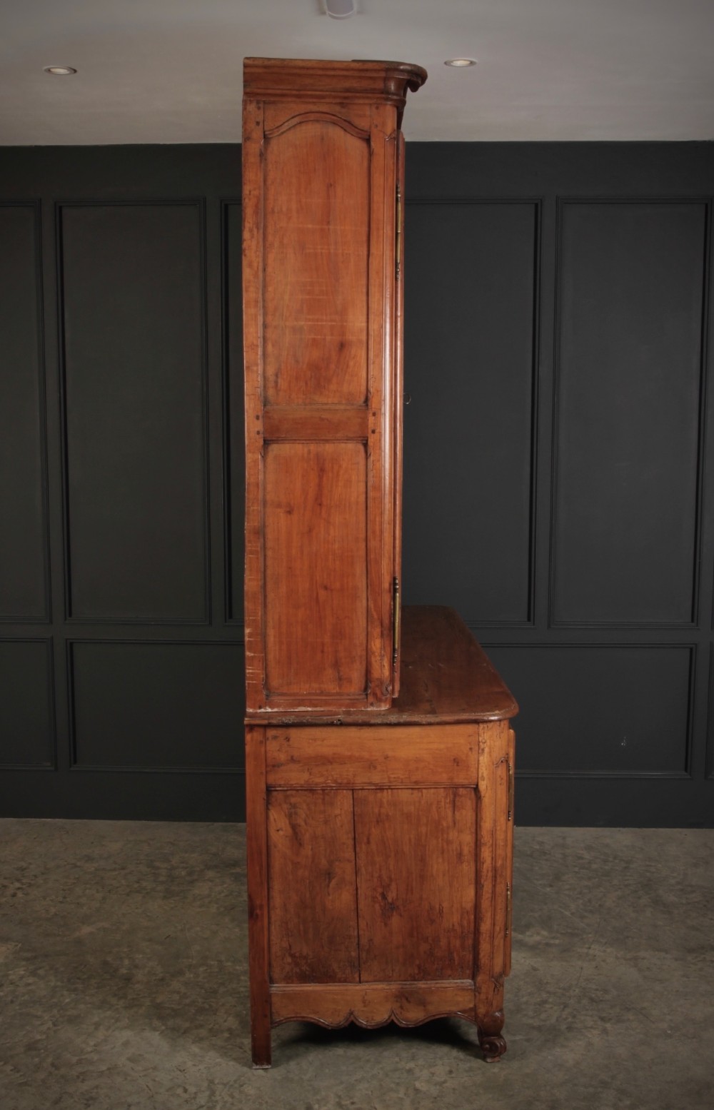 An 18th-century French Provincial two-tier cherry wood cupboard featuring moulded panel doors, long brass hinges, and a curved top cornice. View VI