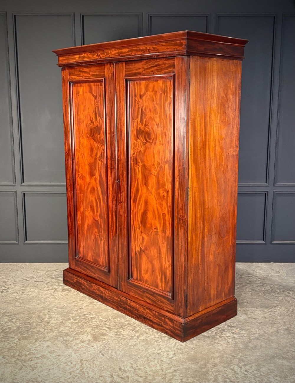 A two-door William IV mahogany wardrobe featuring flame mahogany panels, a moulded top cornice, and a sturdy plinth base. View III