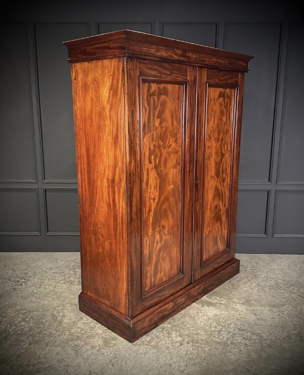 A two-door William IV mahogany wardrobe featuring flame mahogany panels, a moulded top cornice, and a sturdy plinth base.