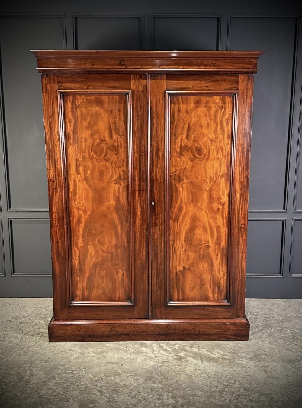 A two-door William IV mahogany wardrobe featuring flame mahogany panels, a moulded top cornice, and a sturdy plinth base. View VII