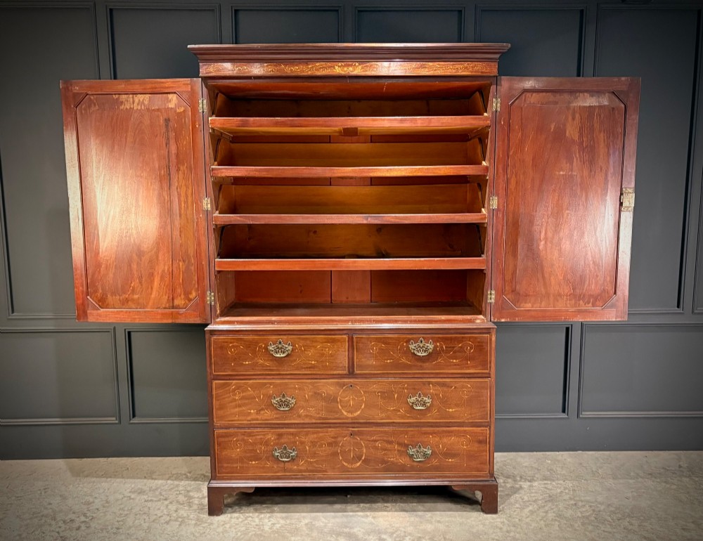 A Georgian mahogany linen press featuring botanical marquetry inlay on upper double doors over four lower drawers with brass handles. View II