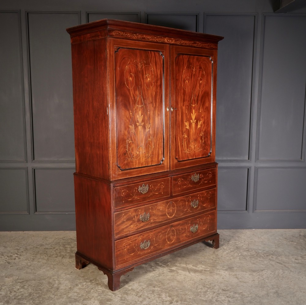 A Georgian mahogany linen press featuring botanical marquetry inlay on upper double doors over four lower drawers with brass handles. View IV
