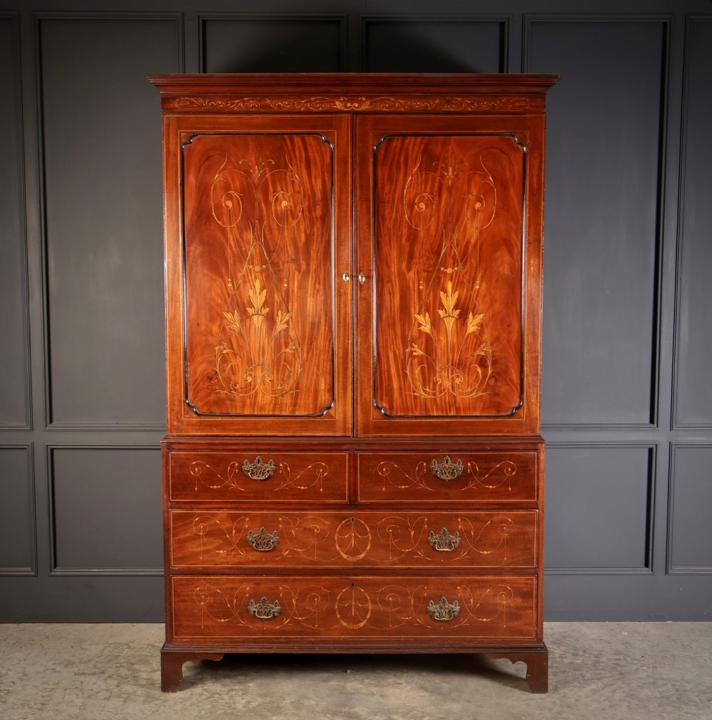A Georgian mahogany linen press featuring botanical marquetry inlay on upper double doors over four lower drawers with brass handles. View V