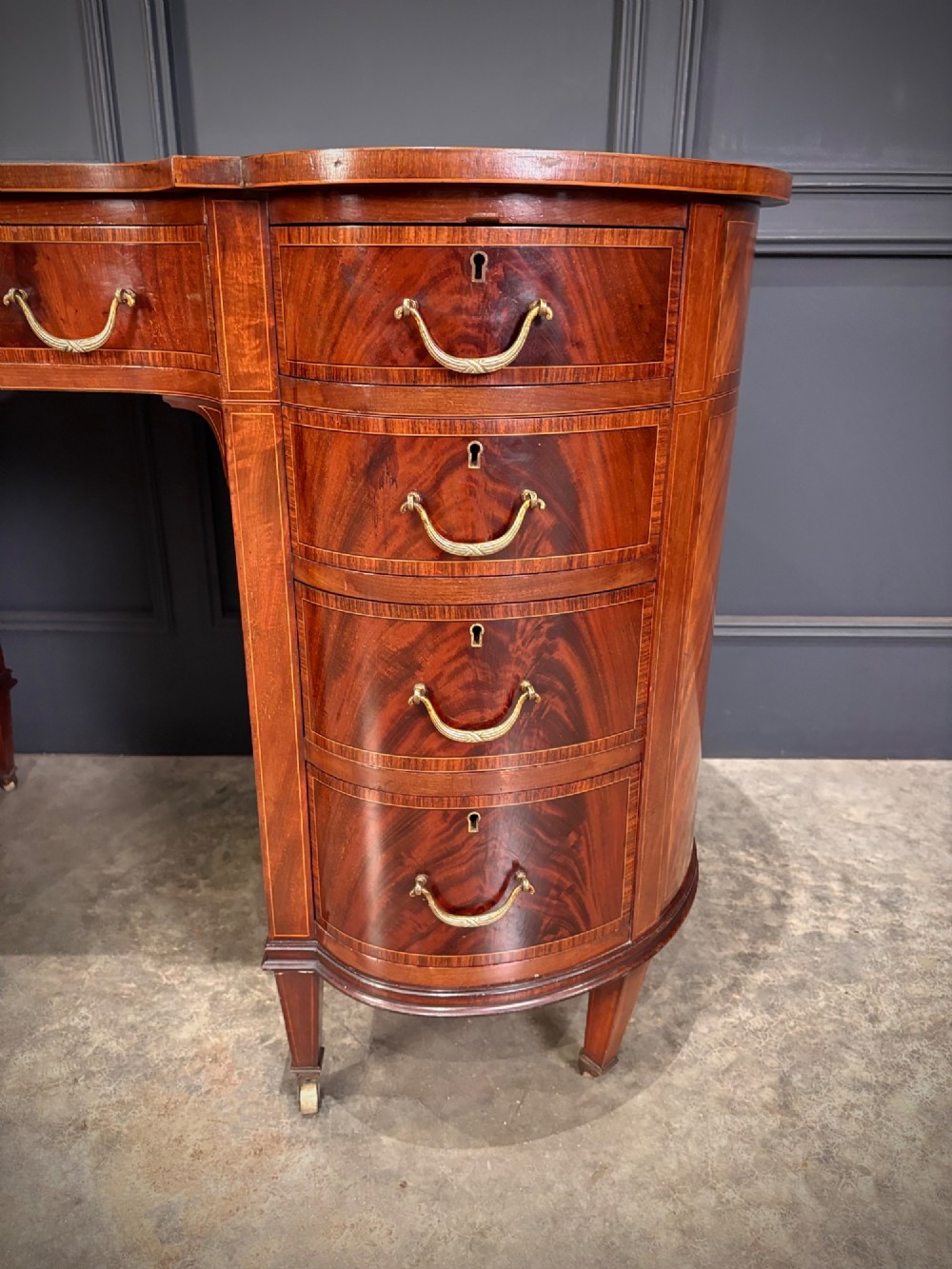 An Edwardian mahogany kidney-shaped writing desk with an inset green leather top, satinwood inlay, curved drawers, brass handles, and tapered legs on castors. View III