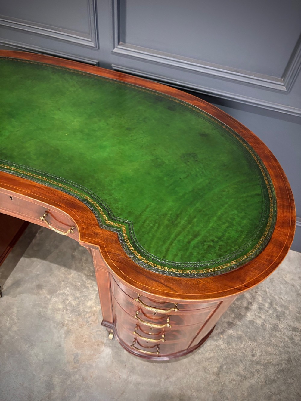 An Edwardian mahogany kidney-shaped writing desk with an inset green leather top, satinwood inlay, curved drawers, brass handles, and tapered legs on castors. View IV