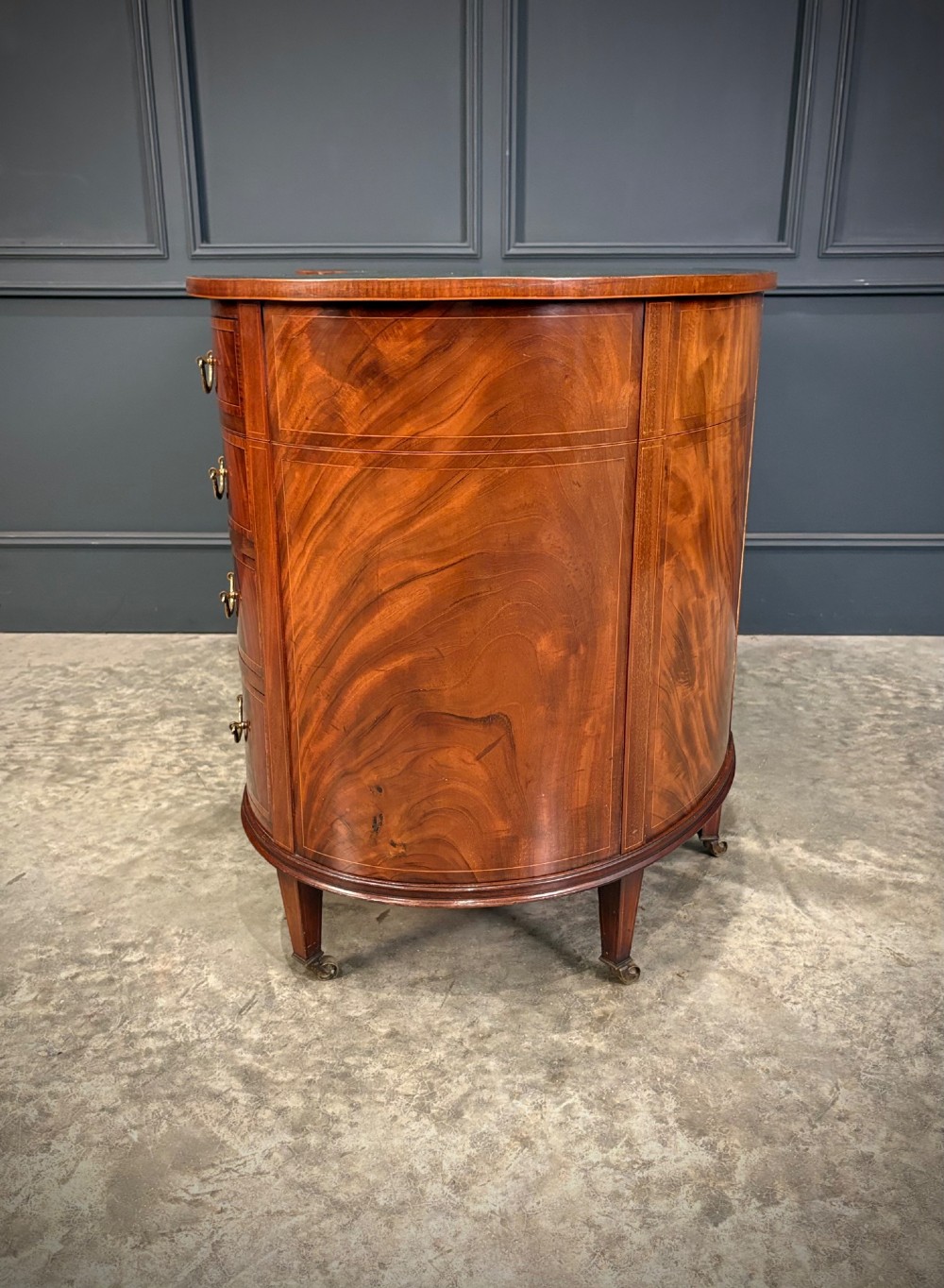 An Edwardian mahogany kidney-shaped writing desk with an inset green leather top, satinwood inlay, curved drawers, brass handles, and tapered legs on castors. View VII