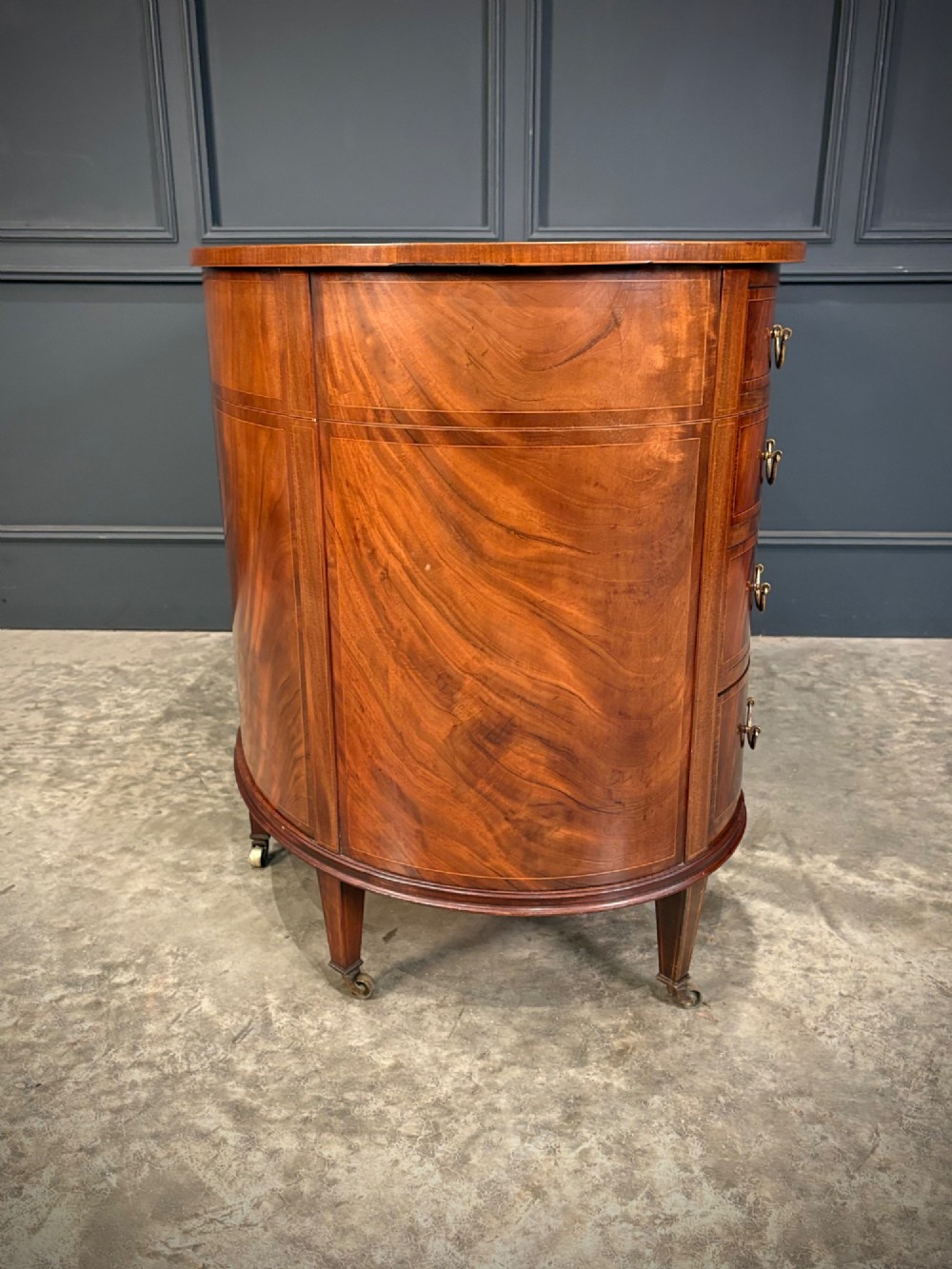 An Edwardian mahogany kidney-shaped writing desk with an inset green leather top, satinwood inlay, curved drawers, brass handles, and tapered legs on castors. View IX