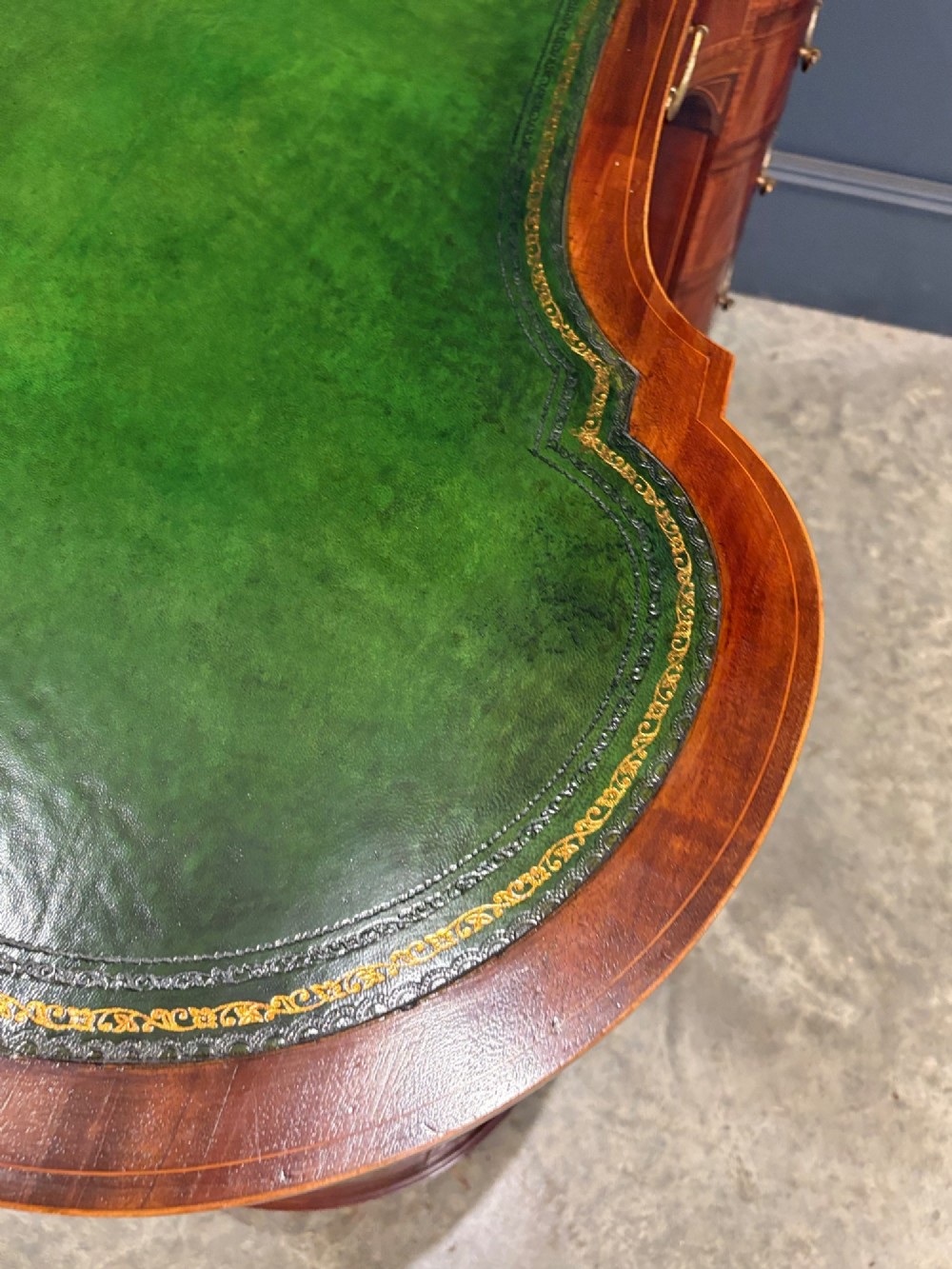 An Edwardian mahogany kidney-shaped writing desk with an inset green leather top, satinwood inlay, curved drawers, brass handles, and tapered legs on castors. View X