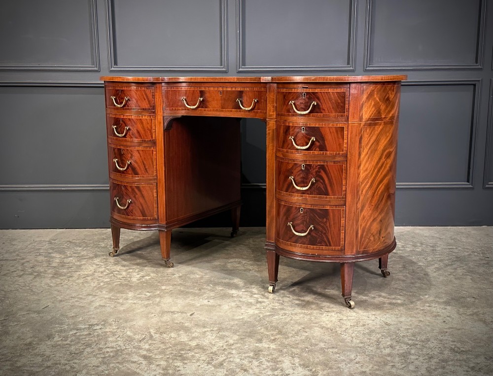 An Edwardian mahogany kidney-shaped writing desk with an inset green leather top, satinwood inlay, curved drawers, brass handles, and tapered legs on castors. View XII