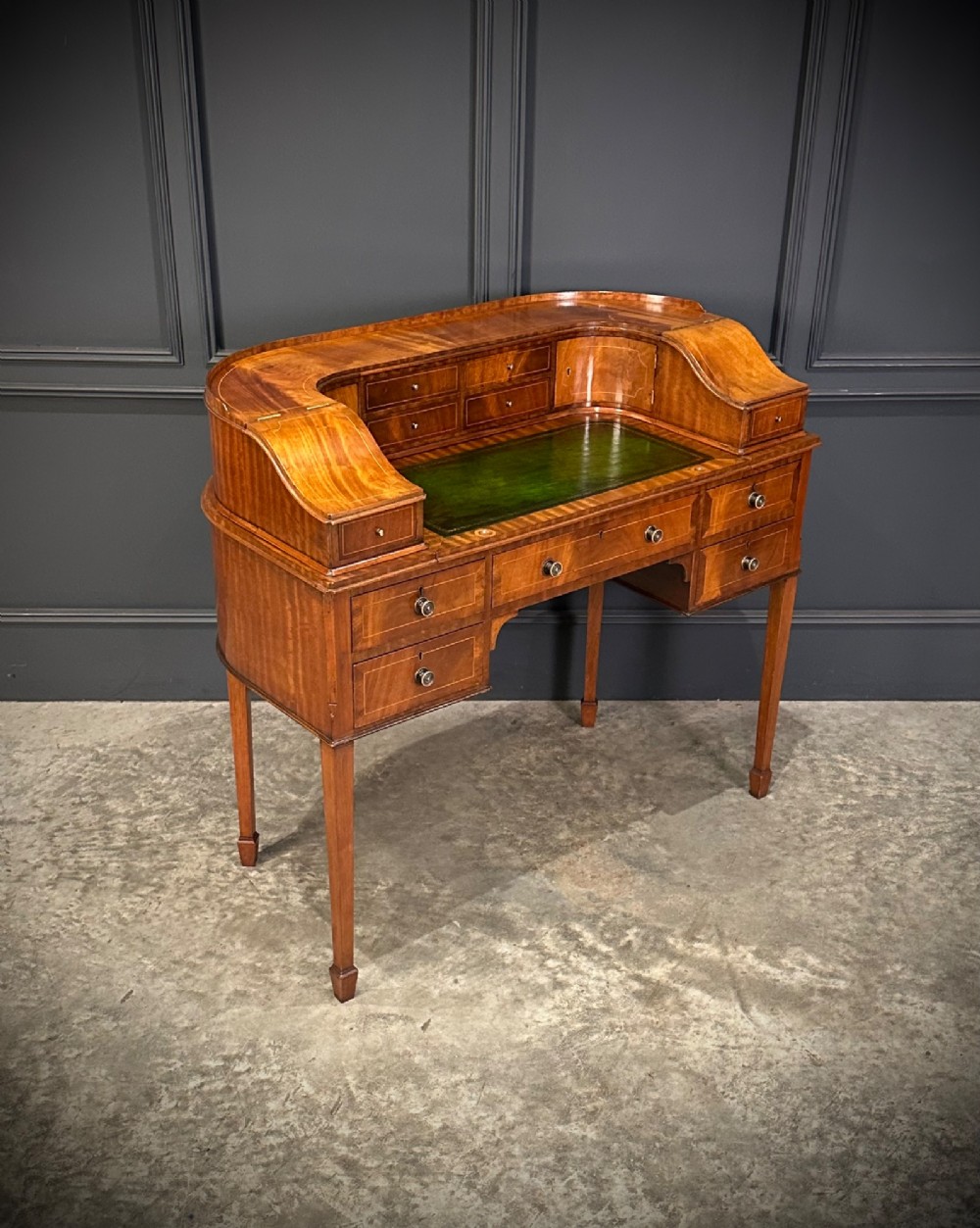 An inlaid mahogany Carlton House writing desk featuring a curved gallery with small drawers and cupboards above a green leather writing surface and square tapered legs. View II