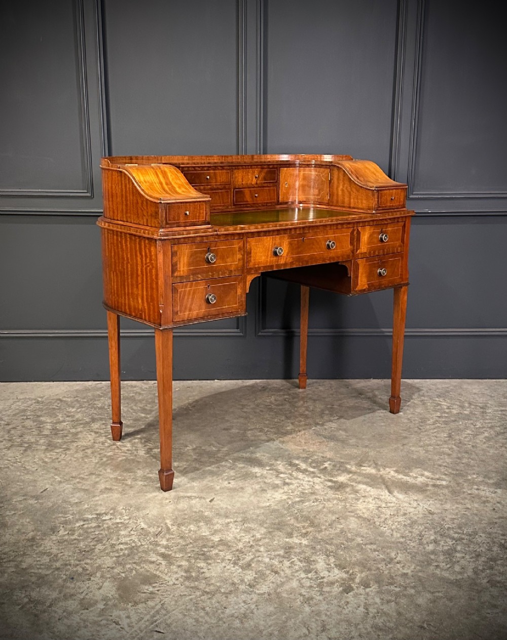 An inlaid mahogany Carlton House writing desk featuring a curved gallery with small drawers and cupboards above a green leather writing surface and square tapered legs.