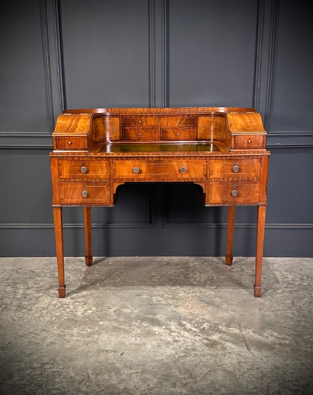 An inlaid mahogany Carlton House writing desk featuring a curved gallery with small drawers and cupboards above a green leather writing surface and square tapered legs. View IV