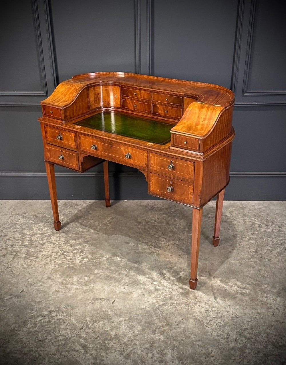 An inlaid mahogany Carlton House writing desk featuring a curved gallery with small drawers and cupboards above a green leather writing surface and square tapered legs. View V