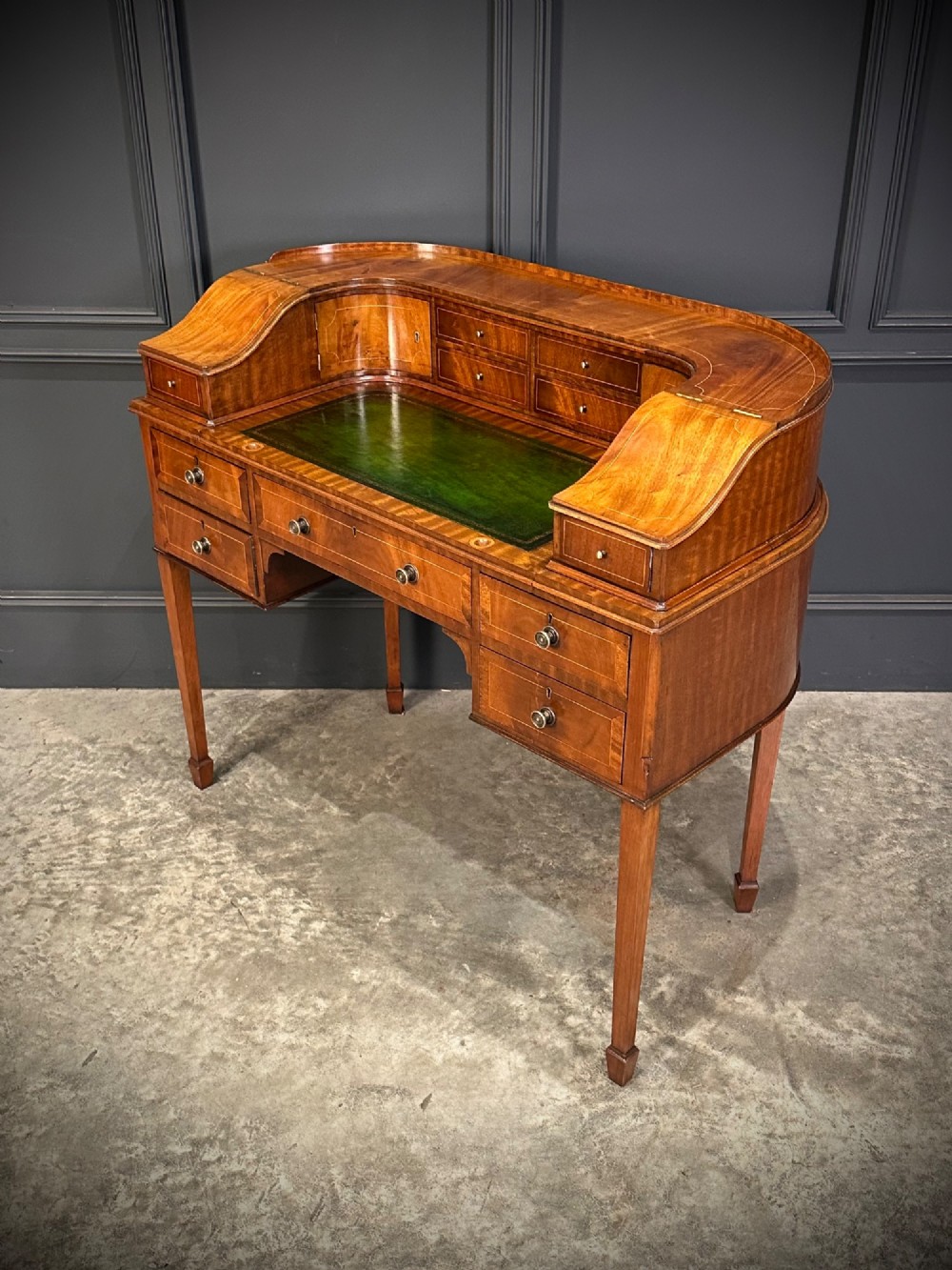 An inlaid mahogany Carlton House writing desk featuring a curved gallery with small drawers and cupboards above a green leather writing surface and square tapered legs. View VI