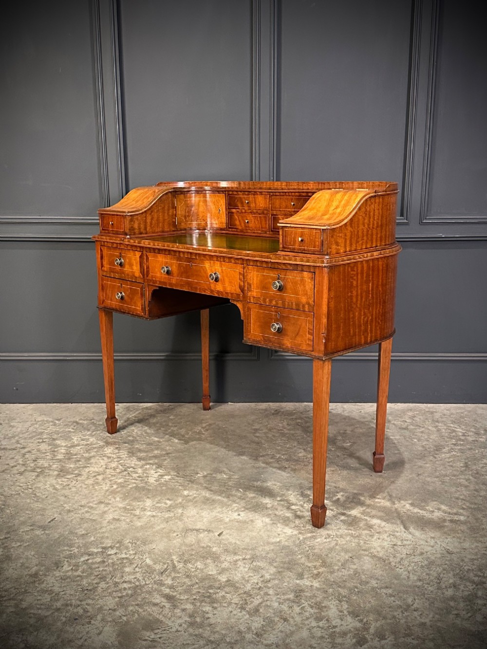 An inlaid mahogany Carlton House writing desk featuring a curved gallery with small drawers and cupboards above a green leather writing surface and square tapered legs. View VII